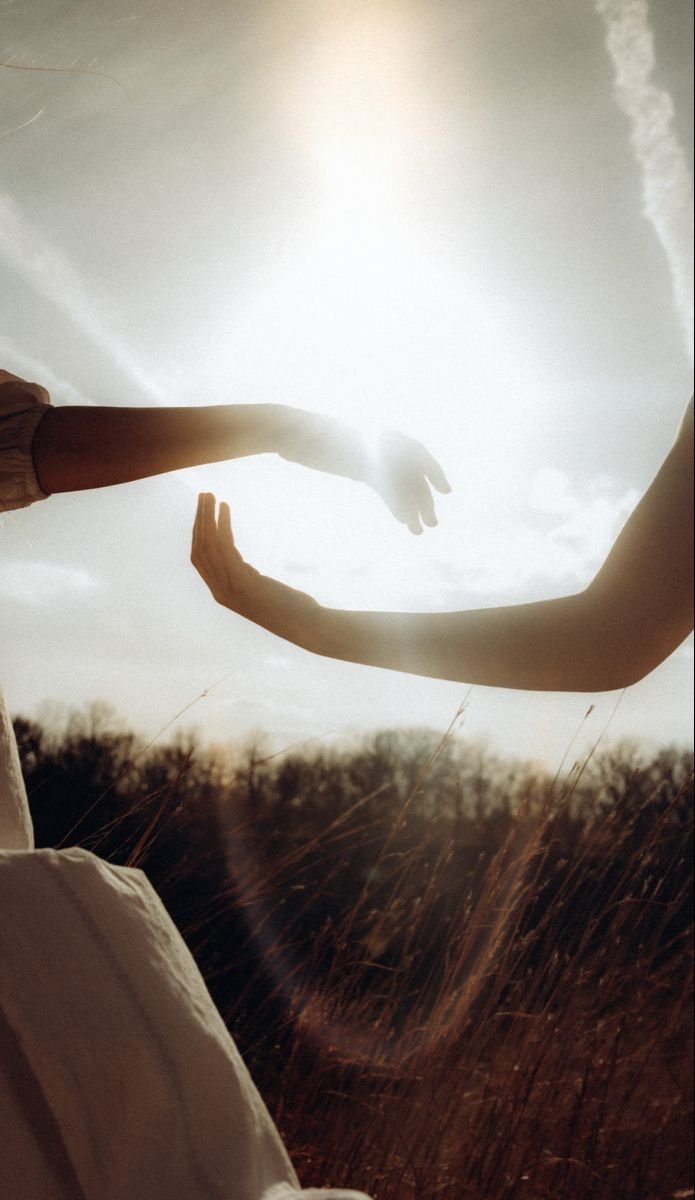 Two hands reaching toward each other at sunset.