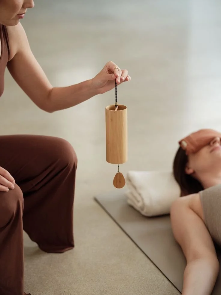Practitioner holding a wooden koshi chime over a client resting on a mat.